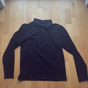 Svart långärmad skjorta från Riley - Klassisk svart långärmad skjorta från Riley med krage och knappar framtill. Skjortan har en stilren look och är perfekt för dig som gillar enkel och tidlös design. Tillverkad i mjukt material som känns skönt mot huden.