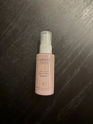 Lumene Dewy Glow Setting Spray - Fräsch ansiktsspray från Lumene i serien Invisible Illumination. Dewy Glow Setting Spray ger en naturlig lyster och fixerar makeupen. Kommer i en ljusrosa plastflaska med spraymunstycke. Passar alla hudtyper och är perfekt för att boosta glowet under dagen.