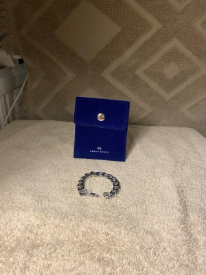 Silverfärgat kedjearmband Urban Story - Snyggt och stilrent armband i silverfärgad metall. Armbandet har en chunky kedjedesign och ett klassiskt lås. Perfekt accessoar för att lyfta din outfit och levereras i en blå sammetsask med knappstängning.