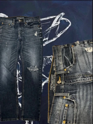 Blå distressed Levi’s Signature jeans - Säljer ett par blå jeans från Levi’s Signature med slitna detaljer och snyggt tvättad look. Jeansen har raka ben, klassiska fem fickor och guldfärgade knappar. Materialet är robust denim i bomull och passformen är normal.