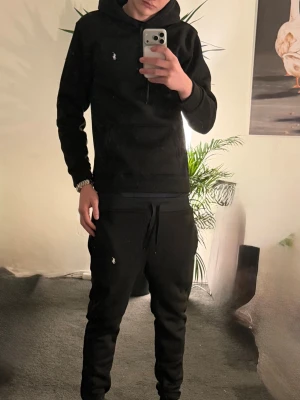 Ralph Lauren track suit - Säljer en svart byxor och holdie från Ralph Lauren med den klassiska vita broderade loggan på bröstet. Perfekt för dig som gillar stilrena och tidlösa plagg.