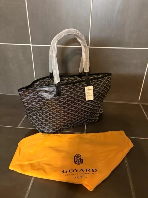 Svart handväska  - Säljer exklusiv fransk lyxväska med det klassiska handmålade chevron-monogrammet (Y-mönster), känt för sin tidlösa design och höga kvalitet. Väskan är tillverkad i det ikoniska belagda canvasmaterialet med detaljer i äkta läder.  Väskan är i mycket fint skick, med välbevarade kanter och ren insida. En lätt, rymlig och elegant modell som passar både till vardag och resa – ett självklart val för den som uppskattar diskret lyx. Det följer med även dast bag.