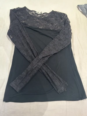 Svart spetsblus från H&M - Säljer en svart långärmad blus från H&M med transparent spets upptill och på ärmarna. Blusen har rund halsringning och blommönstrad spets som ger en elegant vibe. Perfekt att styla med jeans eller kjol för en snygg look.💞💞