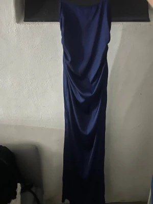 Marinblå långklänning i satin från Nelly - Snygg marinblå långklänning i satin från Nelly. Klänningen har en elegant, slät siluett och är perfekt för dig som vill sticka ut med en stilren look. Materialet är glansigt och följsamt vilket ger en lyxig känsla.