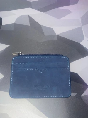 Blå kortplånbok från SEONYU - Snygg blå plånbok från SEONYU i skinnimitation med dragkedja upptill, flera kortfack och ett genomskinligt fack på baksidan för ID eller busskort. Perfekt storlek för fickan och stilren design med kontrastsömmar. Oanvänd