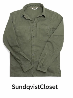 Grön overshirt - Snygg olivgrön overshirt i med klassisk krage och två bröstfickor. Skjortan har långa ärmar och knäppning framtill. Perfekt för lager på lager och ger en avslappnad men trendig look. Storlek 13-14 år