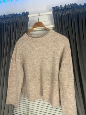 Beige stickad tröja med loose fit - Mysig beige stickad tröja med rund hals och avslappnad, lite boxig passform. Tröjan har långa ärmar och ribbade muddar vid hals, ärmslut och nederkant. Perfekt för lager på lager under kyliga dagar.