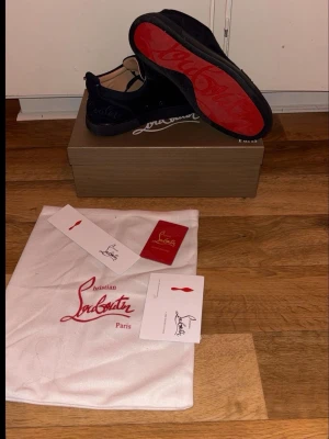 Marinblåa sneakers från Christian Louboutin - Säljer ett par svarta sneakers från Christian Louboutin i mocka. Skorna är marinblåa och har används men fortfarande fräscha. En knapp till lufthålet på vänster sko som man ser i 3e bilden saknas men inget som märks tydligt eller gör skon sämre. 
