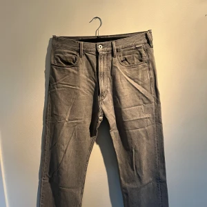 Grå jeans från G-Star RAW - Snygga grå jeans från G-Star RAW med klassisk femficksdesign och raka ben. Jeansen har en diskret logotyp på bakfickan och en silverfärgad patch vid midjan. Materialet är mjukt denim och passformen är normal med midwaist.