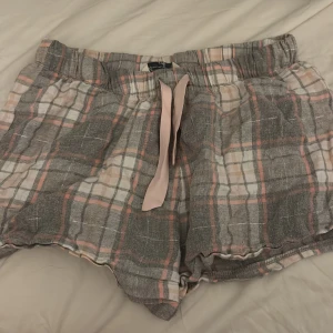 Rutiga shorts med snörning Amazing - Säljer ett par mjuka rutiga shorts från Amazing i grått, vitt och rosa. De har elastisk midja och en ljusrosa snörning framtill. Perfekta för chill dagar och har en loose passform. Materialet känns som bomull och är riktigt skönt mot huden.