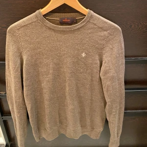 Beige brun merinoulltröja från Morris XS - Snygg beige brun stickad tröja från Morris i 100% merinoull. Klassisk rund hals och långärmad modell med diskret broderad logga på bröstet. Perfekt för dig som gillar stilrena och mjuka plagg med skön passform.