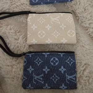 plånbok i beige och blått - Två snygga plånböcker med klassiskt monogrammönster. En är beige med vita detaljer och den andra är mörkblå med ljusblå mönster. Båda har dragkedja och en praktisk handledsrem. Perfekt för att hålla koll på kort och cash. 100kr st