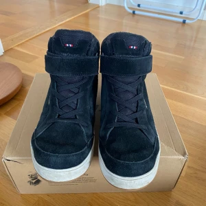 Svarta Viking Eagle Warm GTX sneakers - Svarta Viking Eagle Warm GTX sneakers med högt skaft, snörning och kardborreband. Skorna har en robust gummisula i brunt och är tillverkade i mocka och syntet. Perfekta för dig som vill ha både stil och funktion under höst och vinter.