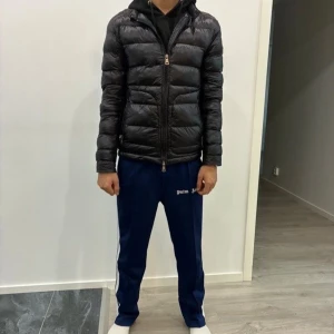 Svart Moncler pufferjacka herr - Säljer en svart pufferjacka från Moncler med klassisk quiltad design och dragkedja framtill. Jackan har lång ärm, hög krage och Moncler-logga på ärmen. Perfekt för kyligare dagar och har en stilren look.