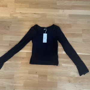 Svart långärmad topp Gina Tricot - En svart långärmad topp från Gina Tricot med rundad halsringning. Enkel och stilren design i mjuk bomull, perfekt att matcha med jeans eller kjol. Säljes med prislapp kvar.