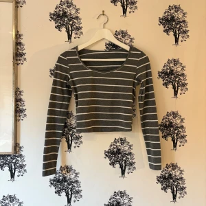 Gråvit randig croppad topp från SHEIN - Grå croppad topp från SHEIN med vita horisontella ränder. Modellen har lång ärm och en rundad halsringning. Tunn och mjuk i materialet, perfekt för att styla med höga jeans eller kjol. Enkel och snygg design som funkar året runt.