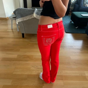 Röda jeans med detaljer  - Snygga röda jeans från Morgan med vit kontrastsöm och coolt silvrigt tigerbroderi på bakfickan. Modellen har låg midja och raka/utsvängda ben. 