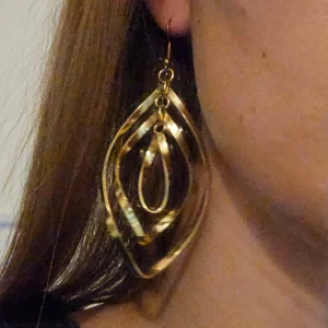 Stora guldiga statement-örhängen - Säljer ett par stora örhängen i guldfärg. De har en modern, böljande form med flera lager i droppdesign. 8 cm långa.