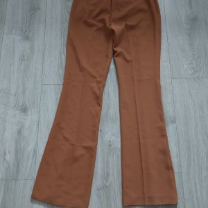 Bruna bootcut kostymbyxor från Mos Mosh - Snygga bruna kostymbyxor från Mos Mosh med bootcut passform och hög midja. Byxorna har pressveck framtill, dold stängning och två bakfickor. Materialet är mjukt och har en lätt stretch för extra komfort. Perfekt för dig som gillar stilrena och trendiga byxor. Stl 34 passar en 34/36 då mos mosh är lite större i stl dyra i inköpa nya, säljes för endast 500kr 