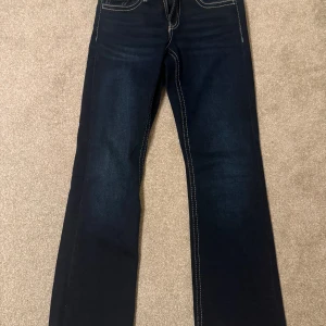 Mörkblå jeans från Gina Tricot - Snygga mörkblå jeans från Gina Tricot med kontrasterande vita sömmar. Modellen har klassiska fem fickor, bakfickor med lock och knappdetalj, samt normal passform. Perfekt för dig som gillar stilrena och tidlösa jeans.