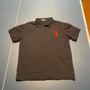 Svart pikétröja från Polo Ralph Lauren - Svart pikétröja från Polo Ralph Lauren med klassisk krage och knappar framtill. 