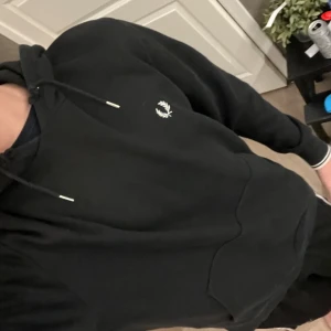 Svart hoodie från Fred Perry - Svart hoodie från Fred Perry med klassisk logga broderad på bröstet. Tröjan har huva med snörning, stor magficka och ribbade muddar vid ärmslut och nederkant. Perfekt för chill dagar och enkel att matcha med jeans eller joggers. Skick 7/10