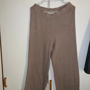 Ribbade stickade byxor från 157, M - Mysiga ribbade byxor i beige från 157. De är stickade och har en relaxed fit med raka ben och bred resår i midjan. Perfekta för chill dagar eller när du vill vara extra bekväm. Snyggt ribbat material som ger en trendig look.