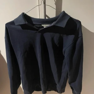 Mörkblå pikétröja från H&M - Snygg mörkblå pikétröja från H&M med klassisk krage och långa ärmar. Tröjan är tillverkad i mjuk bomull och har en enkel, stilren look som passar perfekt till jeans eller chinos. Perfekt för dig som gillar en clean och chill stil.