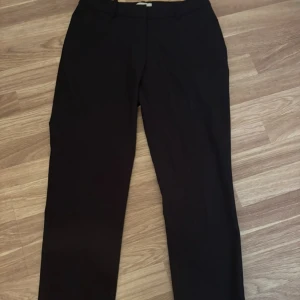 Svarta kostymbyxor från H&M, strl 34 - Klassiska svarta kostymbyxor från H&M i storlek 34. Byxorna har raka ben, bälteshällor och diskreta fickor bak. Perfekt för en clean och stilren look. Materialet är mjukt och har en lätt stretch för extra komfort.
