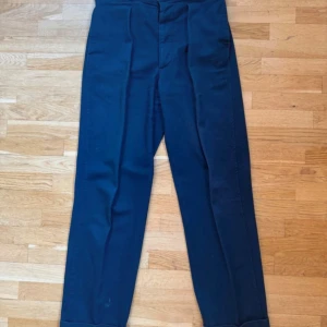 Casatlantic Mogador W32 – navy, hög midja, premium cotton twill - Casatlantic Mogador – klassiska byxor i navy, tillverkade i Portugal av 100 % bomullstwill. Hög midja, enkel frontveck, sidoreglerare och uppvikta benslut ger en tidlös, elegant siluett. Passformen är rak med lätt vidd, inspirerad av 1950-talets skrädderi. Slitstarkt men mjukt tyg som åldras vackert. Mycket bra skick, sparsamt använda. Nypris 1 850 kr.