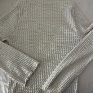 Vit långärmad tröja från 157 - Säljer en vit långärmad tröja från 157 i storlek S. Tröjan har ett vågigt, ribbat mönster över hela ytan som ger en cool textur. Materialet känns mjukt och stretchigt.