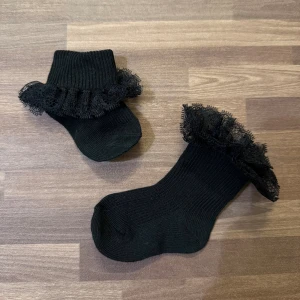 Strumpor med spetskant - Ett par nya, helt oanvända svarta strumpor med spetsvolang runt skaftet. Går att bära som kort eller lång modell med ett vik. Passar 3-12mån.