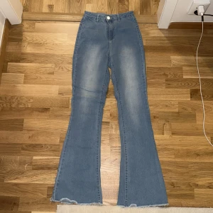 Höjmidja Blå bootcut jeans med rå kant - Snygga högmidja blå bootcut jeans med hög midja och rå, fransad kant längst ner. Jeansen har klassisk femficksdesign, bälteshällor och en knappstängning fram. Materialet är mjukt denim och färgen är ljusblå med lätt tvättade detaljer för en cool look.