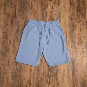 Ljusblå sweatshorts med snörning - Ljusblå sweatshorts med elastisk midja och snörning framtill. Mjukt material, två sidofickor och en bakficka. Perfekta för chill dagar eller träning. Klassisk loose fit och enkel design utan mönster.