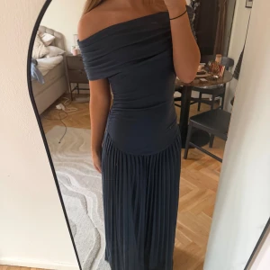 Mörkblå offshoulder långklänning - Säljer en elegant mörkblå långklänning med offshoulder-modell och plisserad kjol. Klänningen har figurnära överdel och axelbandslös design som ger en snygg siluett. Aldrig använd, prislapp kvar! Nypris 1500