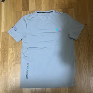 Grå Under Armour tränings-tshirt - Snygg grå t-shirt från Under Armour med färgglatt logotryck på bröstet och tryck på ärmen. Passar S/M