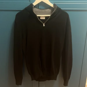 Svart stickad tröja med half zip - Svart stickad tröja från John Henric med half zip-dragkedja vid halsen. Tröjan har lång ärm och ribbade muddar vid ärmslut och nederkant. Perfekt för lager-på-lager och snygg till jeans eller chinos. Den är M men är väldigt anpassbar så passar lite mindre och större. Original pris 1000