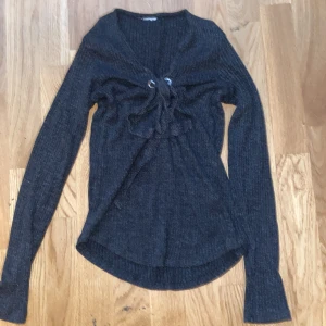 Mörkgrå ribbad stickad tröja med snörning - Säljer en mörkgrå ribbad stickad tröja med snygg snörning framtill. Tröjan har lång ärm och en lite djupare v-ringning. Perfekt för dig som gillar en lite edgy och trendig look. Vet inte vart den är ifrån men köptes någonstans i Sverige iallafall. Har 2 st mindre fläckar kom privat vid snabb affär kan jag sänka priset! 