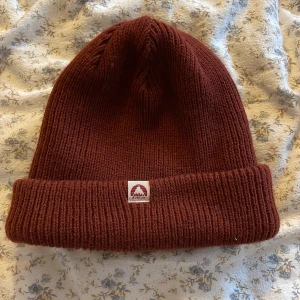 Vinröd stickad mössa från Burton - Snygg tjock,varm vinröd mössa från Burton i ribbstickad modell. Väkdigt skön att ha på sig, knappt använd, fint skick