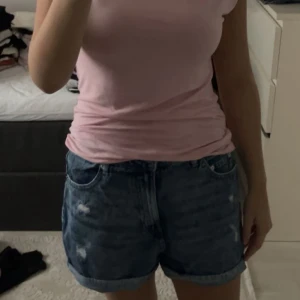 Blå denimshorts med slitningar - Snygga blå jeansshorts med rullade benslut och coola slitningar framtill och baktill. Klassisk femficksmodell med knapp och dragkedja. Perfekta för sommarens alla äventyr, loose fit och skön passform.