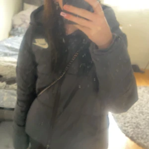 Svart vinterjacka från Nike - Säljer en svart vinterjacka från Nike med vit logga på bröstet. Jackan har huva, dragkedja framtill. Perfekt för kalla dagar och har en clean, sportig vibe. Passar dig som gillar streetwear och vill ha något bekvämt och snyggt.