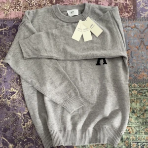 Grå stickad tröja från Ami Paris - En grå stickad tröja från Ami Paris. Tröjan är i väldigt bra skick. Perfekt för dig som gillar stilrena och trendiga plagg.
