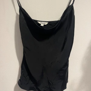 Svart topp med fall i fram - Säljer en svart fest topp med fall i fram och smala axelband. Toppen har v-ringning, den är i ett silkes material och är väldigt bekväm och snygg! 