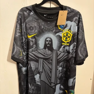 Nike Brasil svart fotbollströja XL - Helt ny snygg svart Brasilien fotbollströja från Nike med unikt grafiskt tryck av Kristusstatyn och brasilianska symboler. Tröjan har korta ärmar, gul CBF-logga och Nike Swoosh, samt är tillverkad i Dri-FIT-material som andas. Perfekt för dig som vill sticka ut på planen.