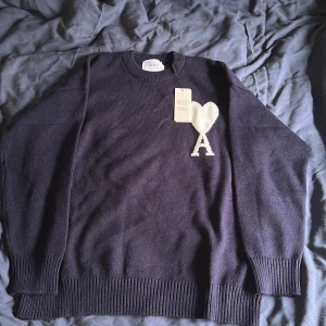 Mörkblå stickad tröja från Ami - Snygg mörkblå stickad tröja från Ami paris med vit hjärt- och A-detalj på bröstet. Tröjan har rund hals, ribbade muddar och lång ärm. Perfekt för dig som gillar stilrena och coola plagg med unik design. Den är helt ny säljer för den är för stor för mig, det är min kompis som har den på i bilden.
