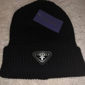 Svart Prada Mössa - 🖤 Snygg och stilren svart Prada-mössa till salu! 🧢 En tidlös favorit som passar till alla tillfällen – perfekt för både vardag, promenader och stadshäng. Den svarta färgen gör den lätt att matcha med allt, samtidigt som Prada-loggan ger en lyxig känsla ✨ Mjukt material och modern design för en trendig men elegant look.