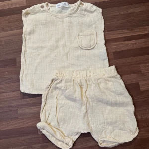 Beige set - Supersöt beige tröja med matchande shorts från Zara i storlek 68 (3-6mån). Muslintyg framme, träknappar i axeln och uppvikta benslut på shortsen. Använt väldigt fåtal gånger och i mycket fint skick, möjligtvis någon tråd som släppt på något ställe men inget som varken syns väl eller påverkar funktionen.