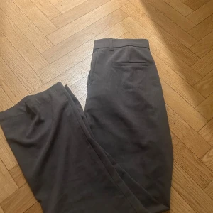 Grå kostymbyxor från 157, storlek S - Snygga grå kostymbyxor från 157 i storlek S. Klassisk rak passform med diskret bakficka och hällor för bälte. Perfekt för dig som gillar stilrena och enkla byxor med modern touch. Materialet känns mjukt och har en lätt stretch.