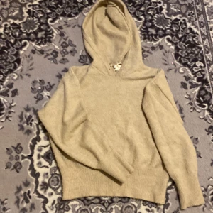 Beige stickad hoodie från Gina Tricot - Mysig beige stickad hoodie från Gina Tricot med huva och ribbade muddar. Perfekt för kyliga dagar och enkel att matcha med jeans eller leggings. Klassisk modell med lång ärm och relaxed fit.