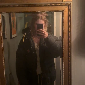 Svart dunjacka från Fjällräven S - Säljer en svart dunjacka från Fjällräven i storlek S. Jackan har huva med gula snören, broderad Fjällräven-logga på bröstet och flera fickor framtill. Den är quiltad och har dragkedja samt knappar. Perfekt för kalla dagar och har en loose passform. (Priset går att diskutera)